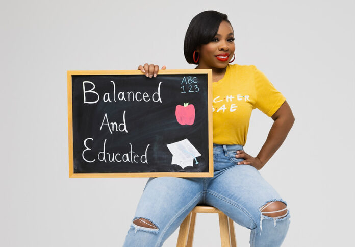 Applemania Bradford - Teacher B.A.E. Applemania Bradford, founder and CEO of Teacher B.A.E., holds a Balanced and Educated chalkboard.